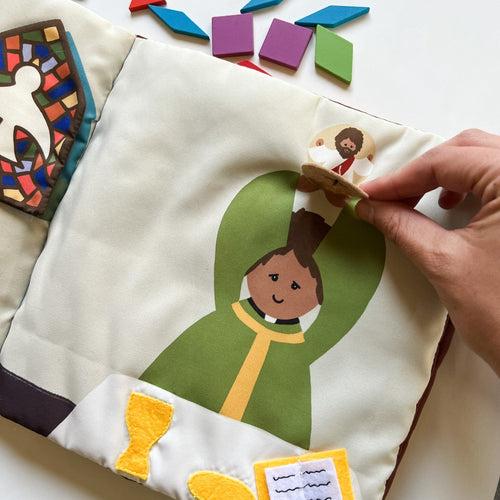 Close-up of fabric page showing priest lifting circular Jesus figure in green robe from interactive Catholic Mass quiet book