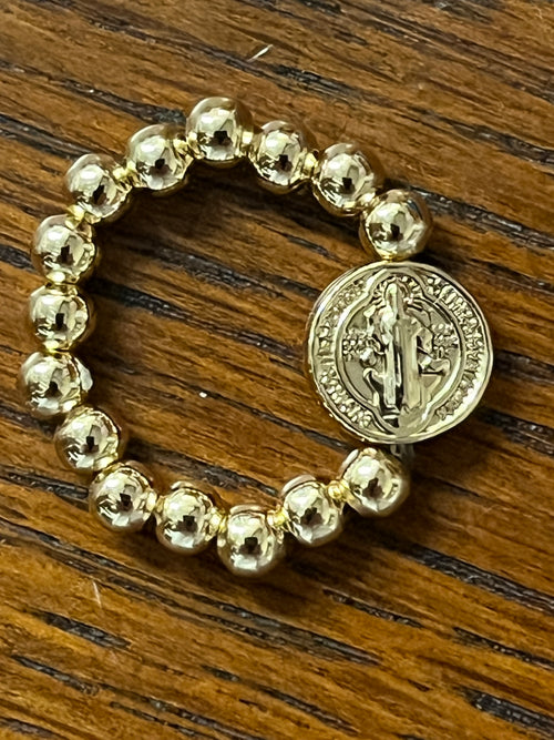 Gold-tone Benedict medal stretch ring with polished round beads on wooden background