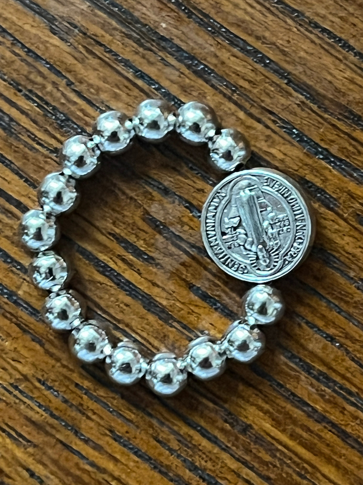 Silver stretch ring with polished round beads and detailed Benedict medal centerpiece on wooden surface