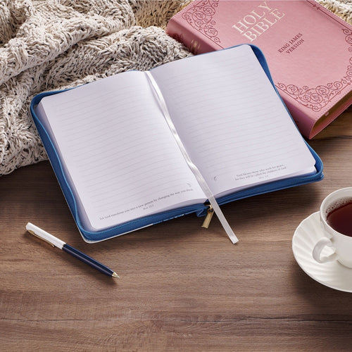 Love Blue Floral Tile faux leather journal with zipper closure open to blank pages, scripture verse, pen, coffee cup, and Bible on table