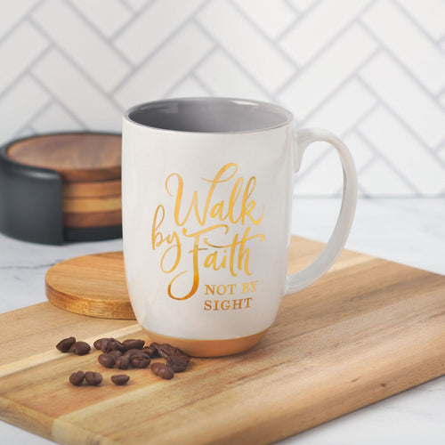 White ceramic coffee mug with gold lettering “Walk by Faith Not by Sight” and exposed clay base on wooden board