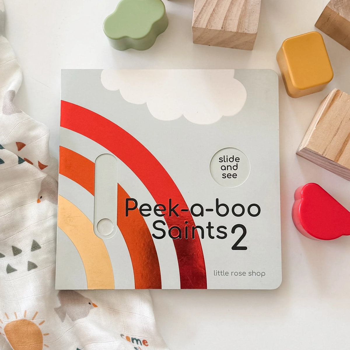 Catholic Peek-a-boo Saints 2 board book with rainbow design and interactive slider for children’s faith learning